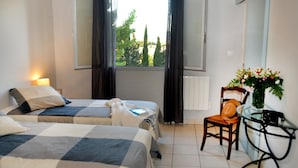 Quarto de hotel com duas camas, uma cadeira, uma mesa e janela com cortinas.