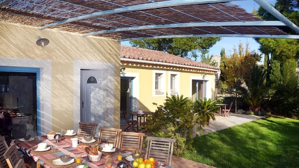 Uma área de refeições ao ar livre com uma mesa posta para refeição, cercada por cadeiras e uma pérgola por cima.