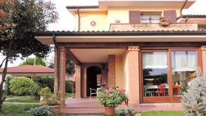 A two-story house with a covered porch, a brick exterior, and a large sliding glass door leading to a dining area. - B&B Dora e Flavio (Montegrotto Terme)