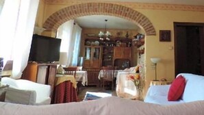 A cozy living room with a TV, a dining area with a chandelier, and a kitchen visible through an archway. - B&B Dora e Flavio (Montegrotto Terme)