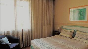 Ein Schlafzimmer mit einem großen Bett, einem Sessel, einem Nachttisch und einem Fenster mit Vorhängen.