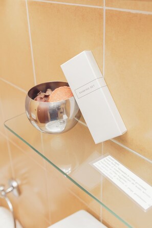 Ein Badezimmer mit einem Glasteil, auf dem eine Metallschüssel und eine weiße Schachtel mit der Aufschrift 'SHAWING SET' stehen.