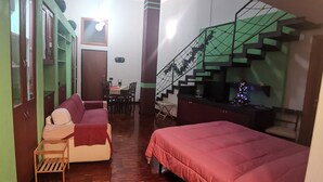 A compact room with a sofa, a bed, and a staircase with a green railing.
