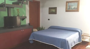 A room with a bed, a desk with a computer, a door, and two framed pictures on the wall. - Palazzo Carafa della Spina - Charme (Naples)