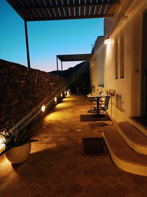 Eine terrasse mit Steinpflaster, einem Tisch, Stühlen, einer Steinmauer und einer Pergola.