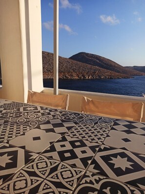 A room with patterned floor tiles, a view of the sea, and a mountainous landscape.