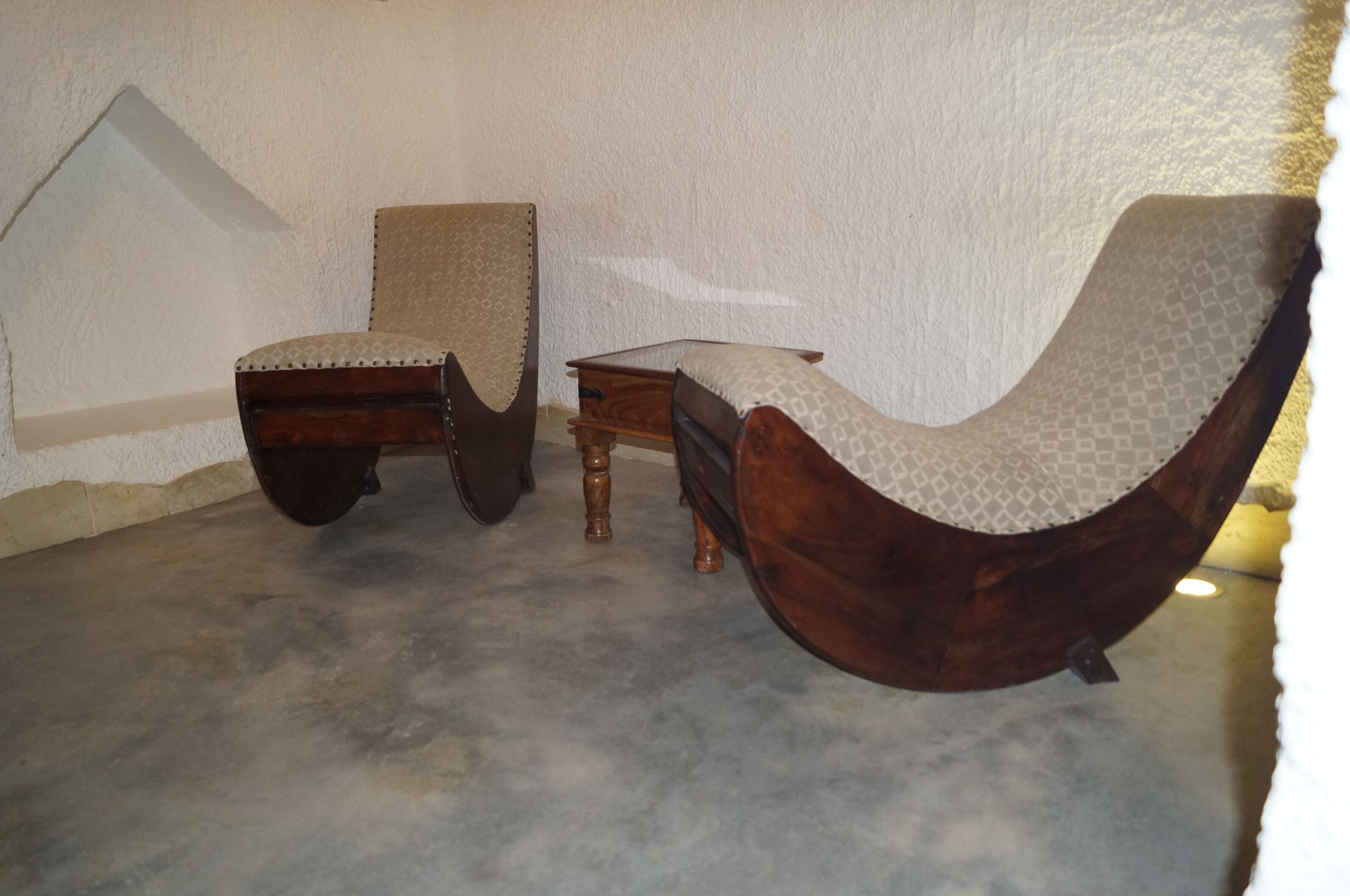 A room with a wooden armchair and a matching ottoman, a small wooden side table, and a patterned armchair.
