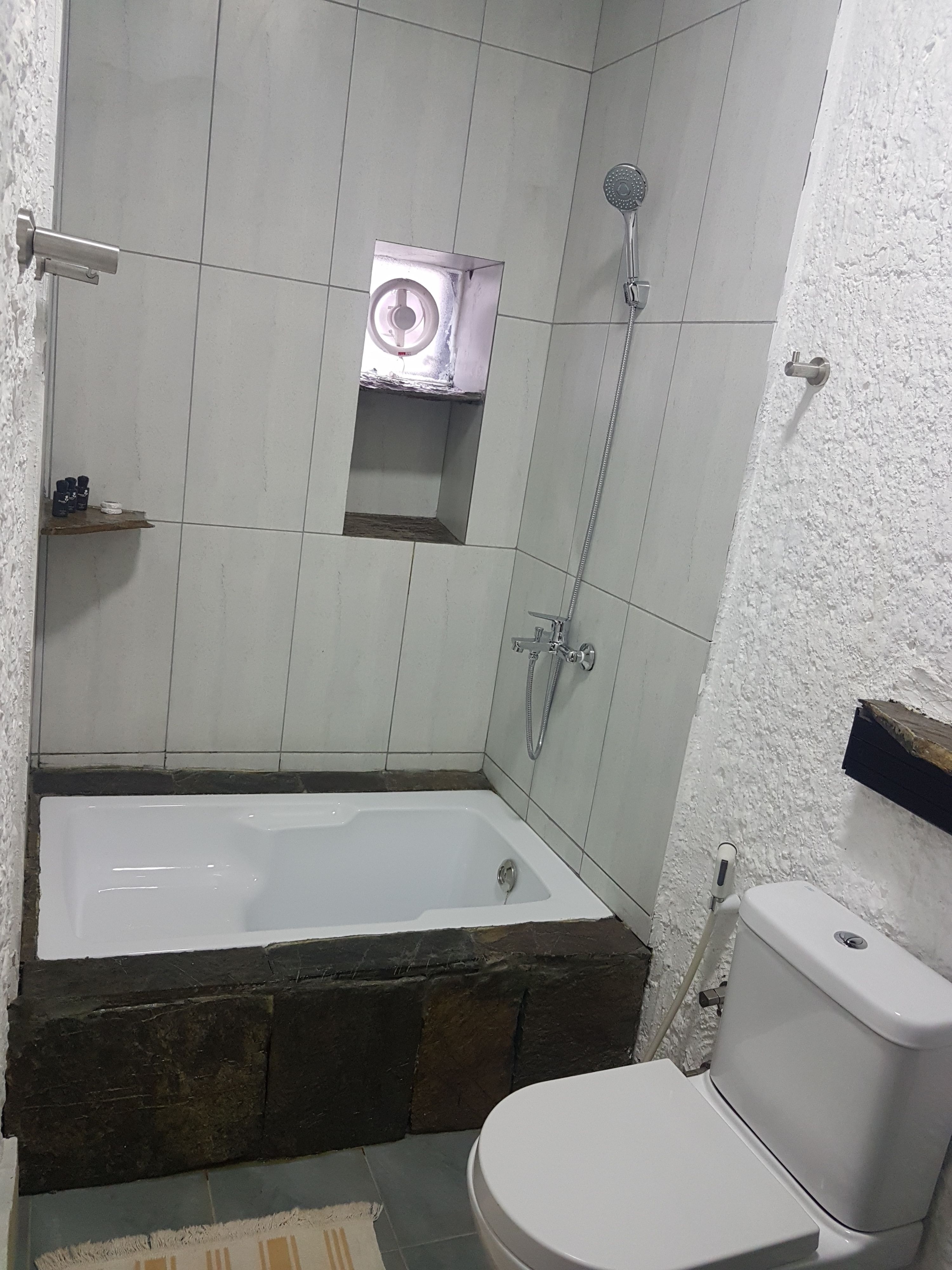 A bathroom with a bathtub, toilet, shower, and a small window.