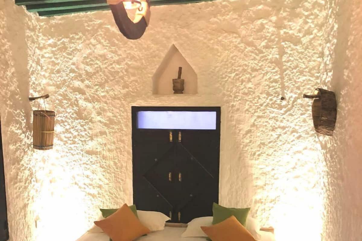 Una habitación con cama, almohadas, un televisor de pared y un estante pequeño con una vela.