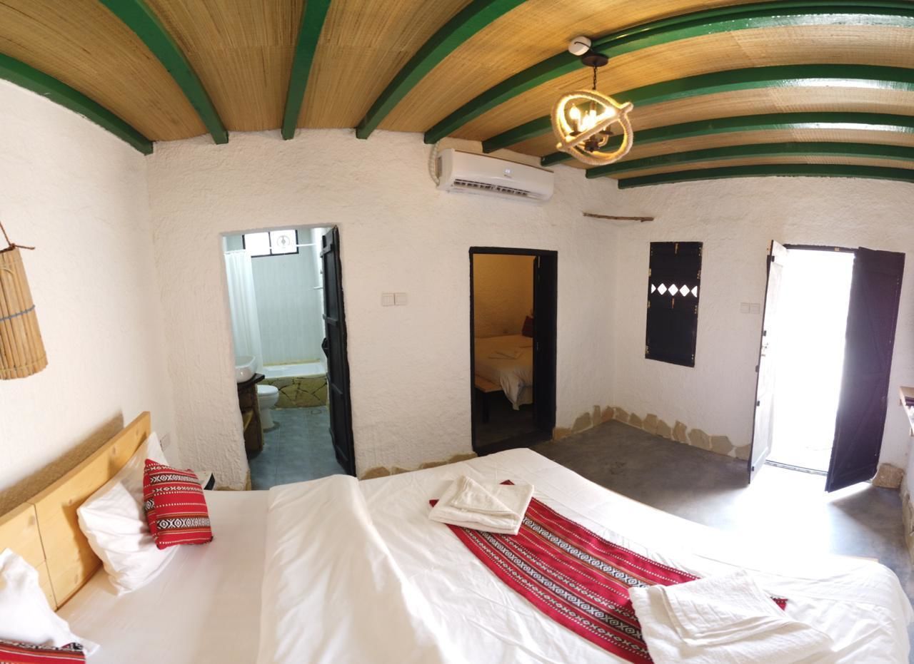A hotel room with a bed, a wooden headboard, an air conditioning unit, and a door leading to another room.