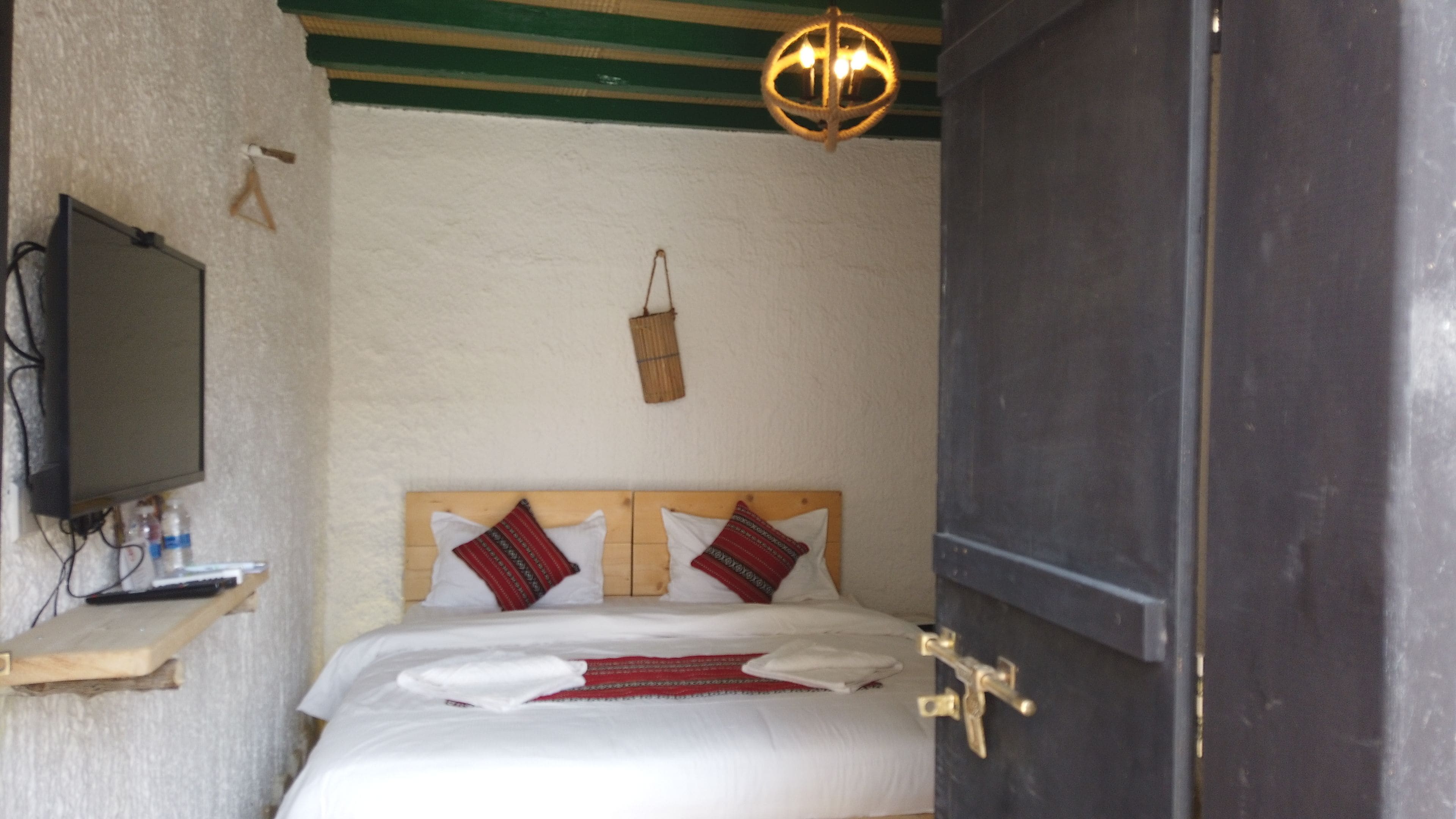 Un dormitorio con una cama, un televisor en una estantería, una cesta colgante y una puerta.