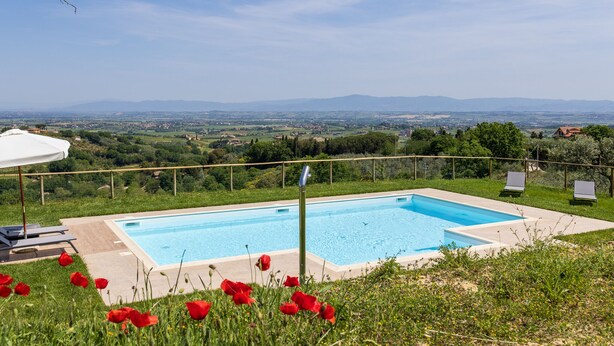 A rectangular swimming pool with a clear blue sky and distant mountains in the background.