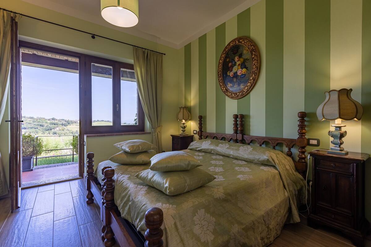 Une chambre avec un grand lit, une vue par la fenêtre et un tableau accroché au mur.