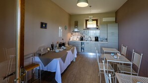 A compact kitchen with a dining area, featuring a table set for two, a hanging light fixture, and a tiled backsplash.