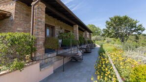 A brick building with a covered patio, outdoor seating, and a garden with yellow flowers.