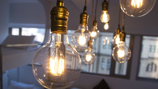 Une pièce avec des ampoules en verre suspendues au plafond, un lit et un mur orné de tableaux encadrés.