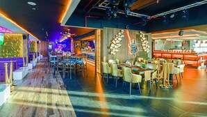 Een modern restaurant met een lange eetzal, meerdere tafels en een bar.