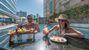 Een zwembadterras met een tafel gedekt voor twee personen, inclusief een fruitschaal en een cocktail.