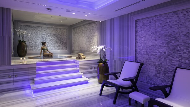 Een moderne spa-ruimte met een marmeren vloer, een zithoek met stoelen, een grote vaas met orchideeën en een stenen muur.