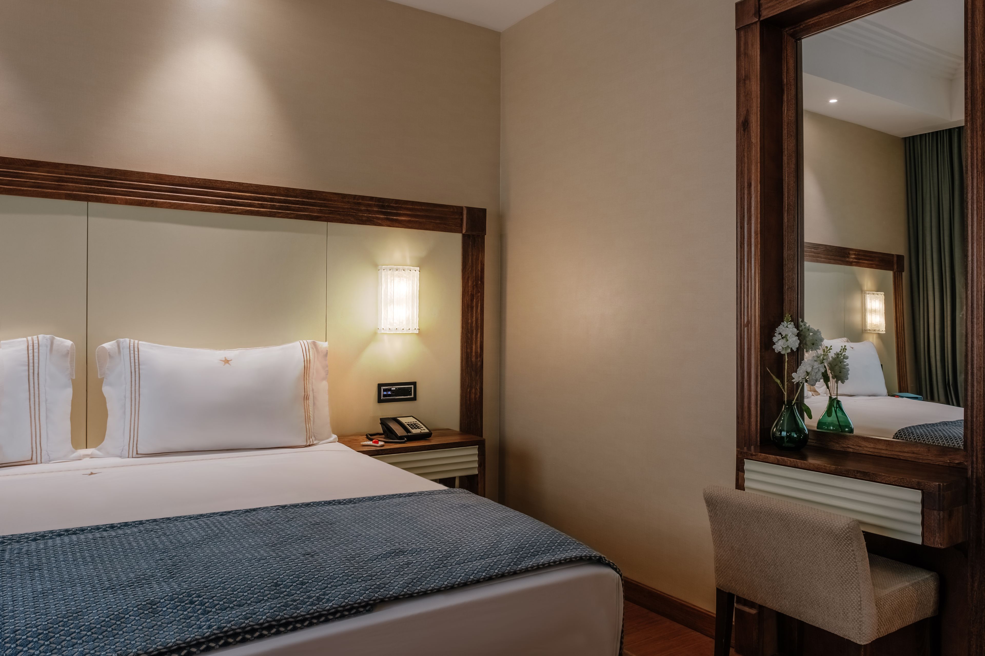 Ein Hotelzimmer mit einem großen Bett, einem Nachttisch mit Lampe, einem Spiegel und einem Sessel.