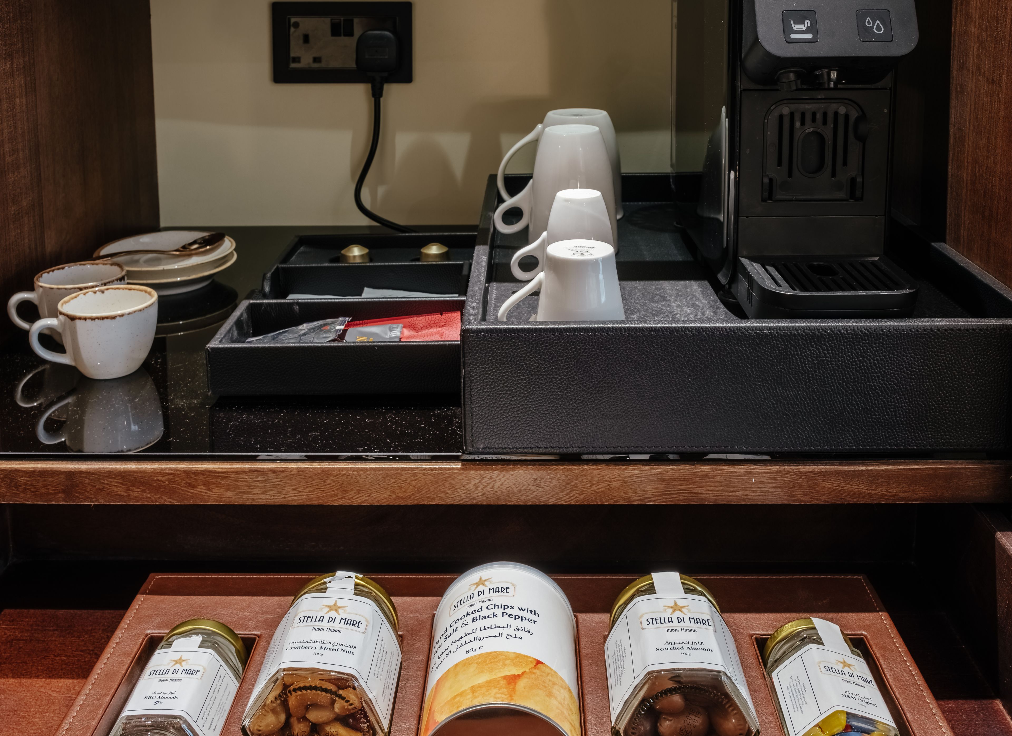 A coffee station with cups, a coffee machine, and a tray with snacks. There are also jars of nuts and almonds.