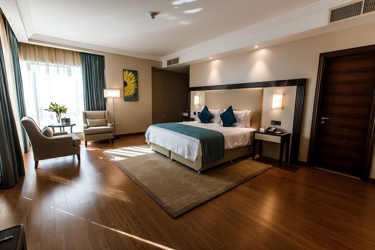 Une chambre d’hôtel avec un grand lit, un bureau avec une lampe, une chaise et une vue sur l’extérieur.