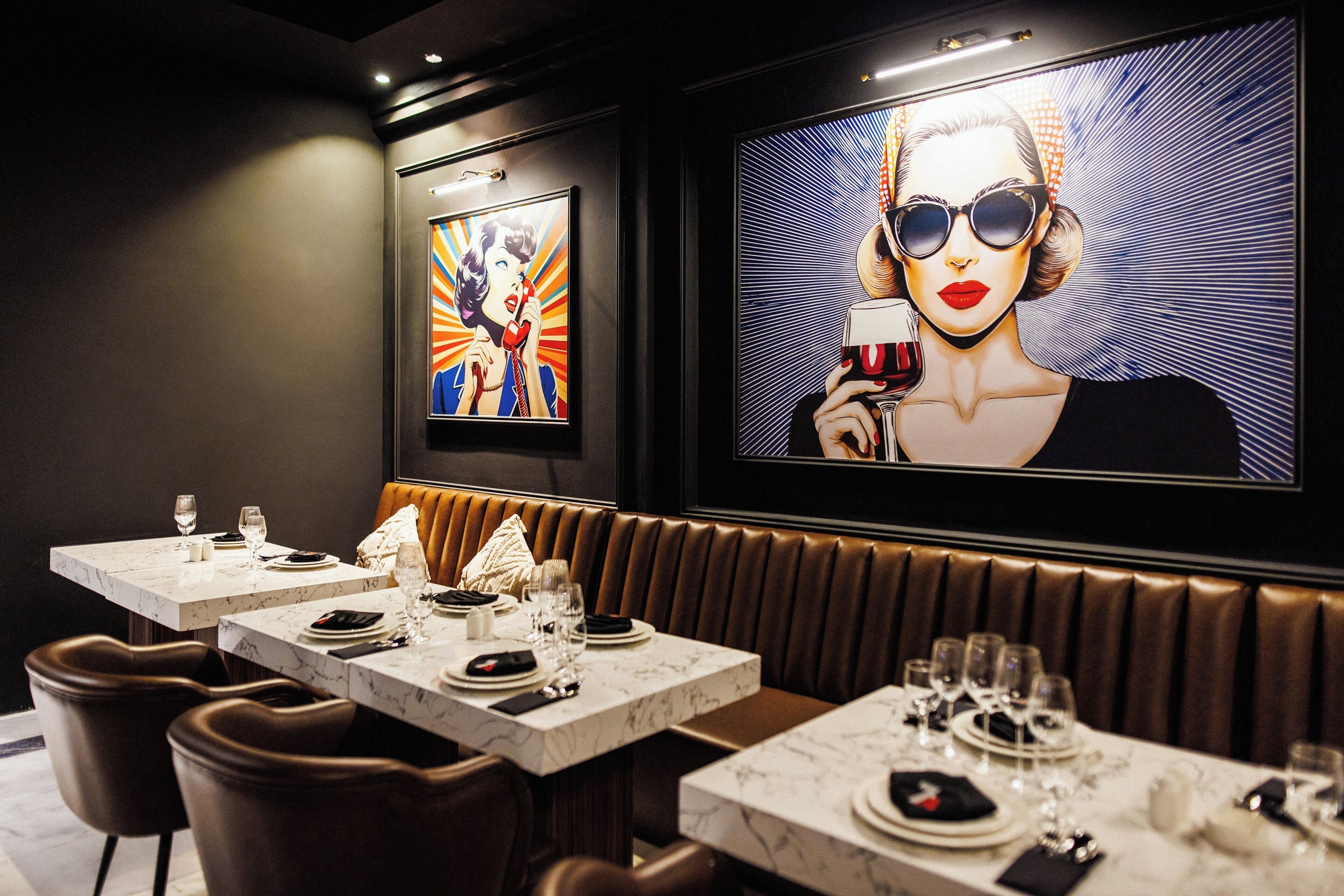 A restaurant with marble-topped tables, brown leather booths, and artwork on the walls.