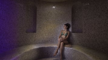 A person sitting in a stone-walled, circular bath area with a small window.