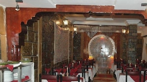 A restaurant with rows of tables and chairs, a red carpet, and a decorative archway. - Hotel Tiout (Taroudant)