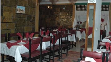 Un restaurant amb parets de pedra, caires vermelles i tovallons blancs.