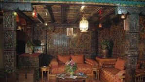 A richly decorated room with a patterned carpet, a sofa, a coffee table with magazines, and a hanging light fixture. - Hotel Tiout (Taroudant)