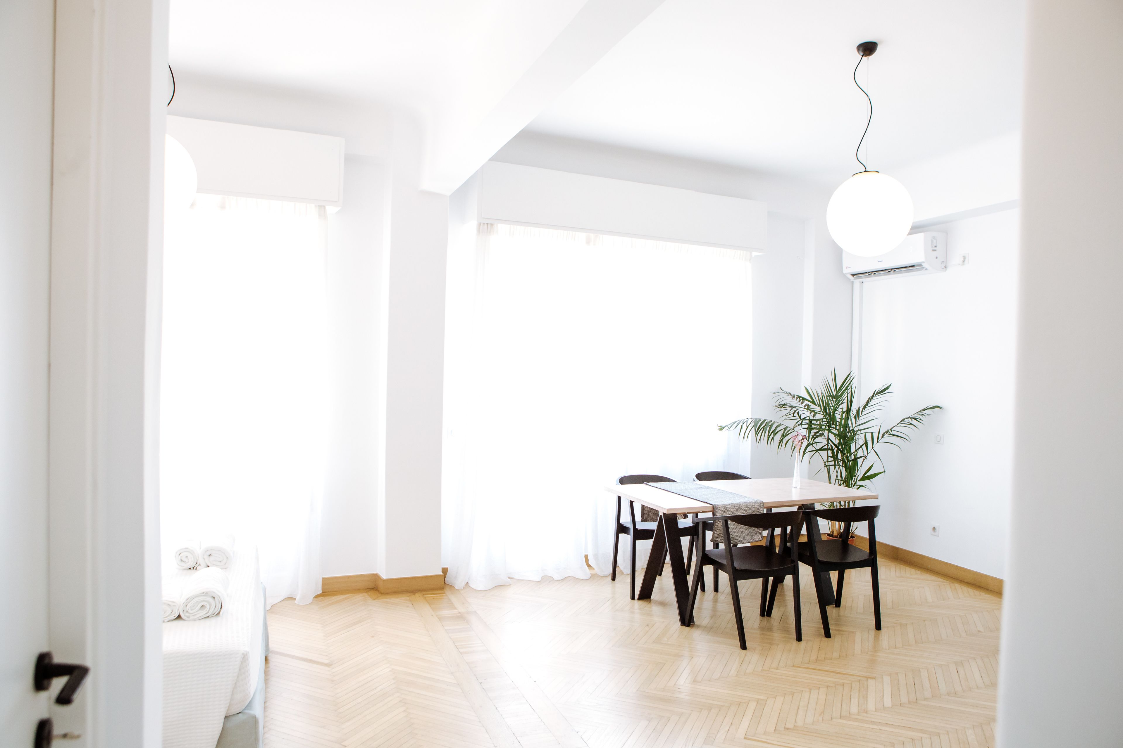 A bright dining area with a wooden herringbone floor, a round table with chairs, and a hanging light fixture.