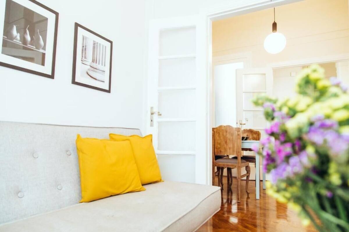 Ein Wohnzimmer mit einer Couch, gelben Kissen und einem Essbereich mit Stuhl und Tisch.