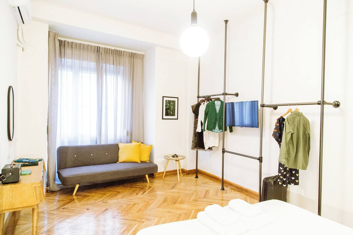 Ein Zimmer mit einer Couch, einem Kleiderständer, einem kleinen Tisch und einem Bett.