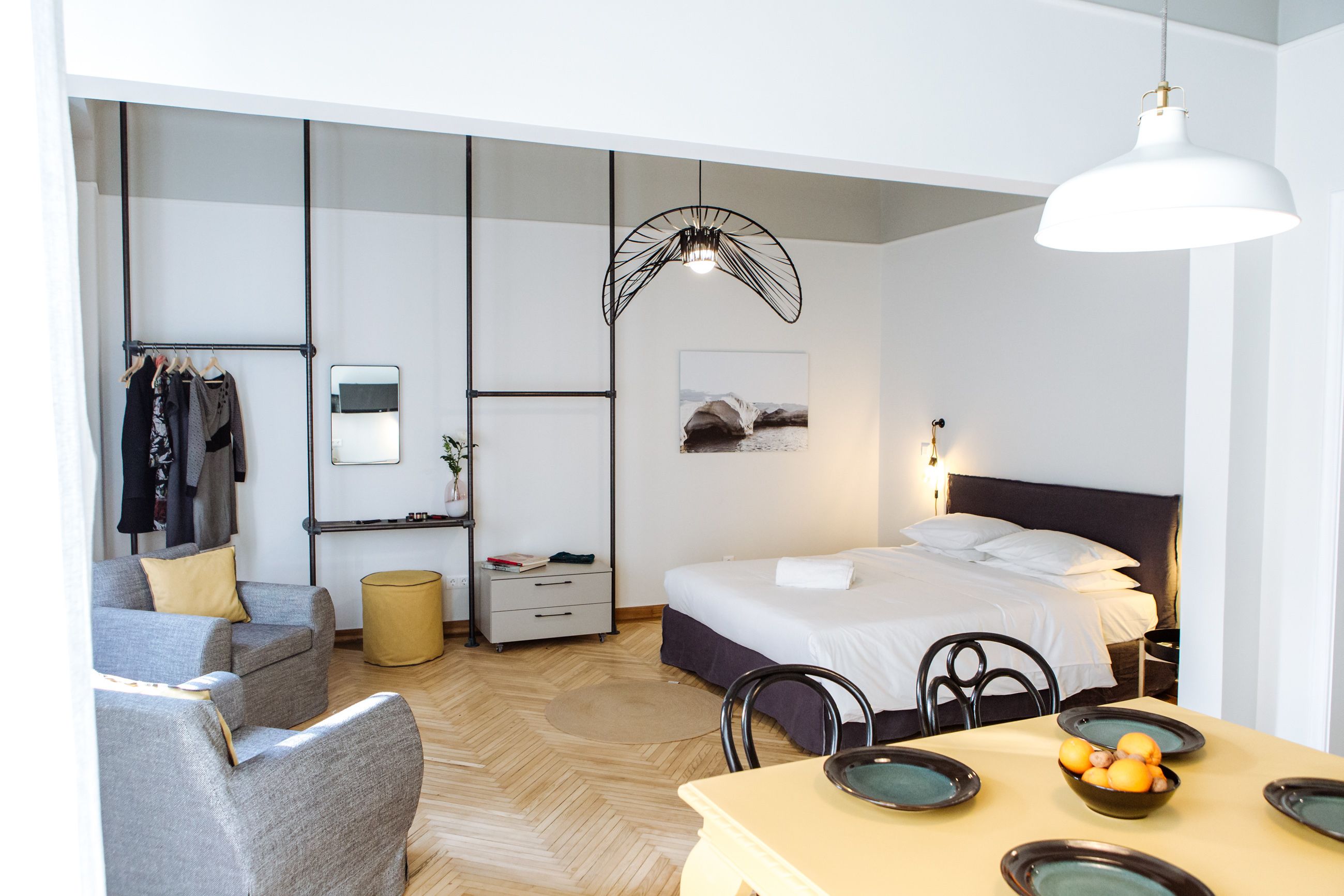 Una habitación de hotel moderna con cama, una mesa de comedor con platos, una silla, un sofá, un espejo, un perchero y una lámpara colgante.
