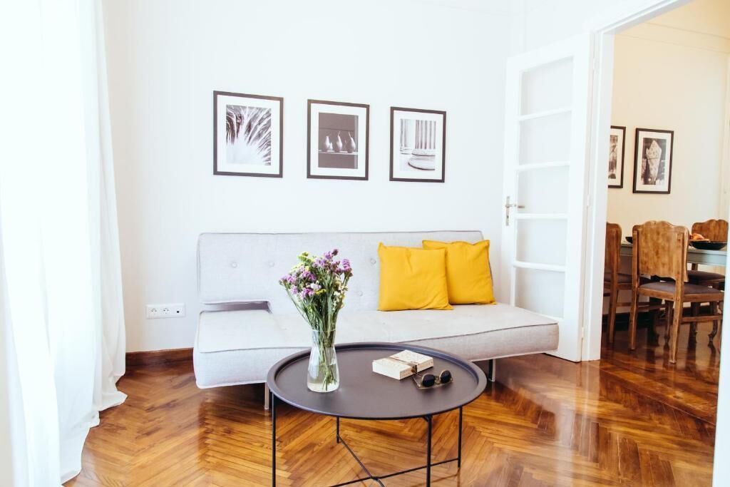 A modern living room with a grey sofa, yellow cushions, a round coffee table with a vase of flowers, and framed pictures on the wall.