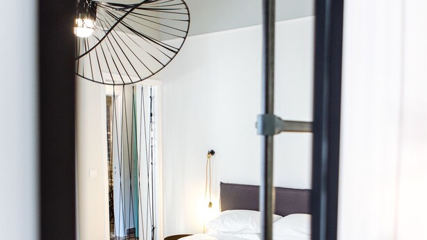 A bedroom with a bed, a mirror, and a hanging light fixture. - We Saw Athens (Athens)