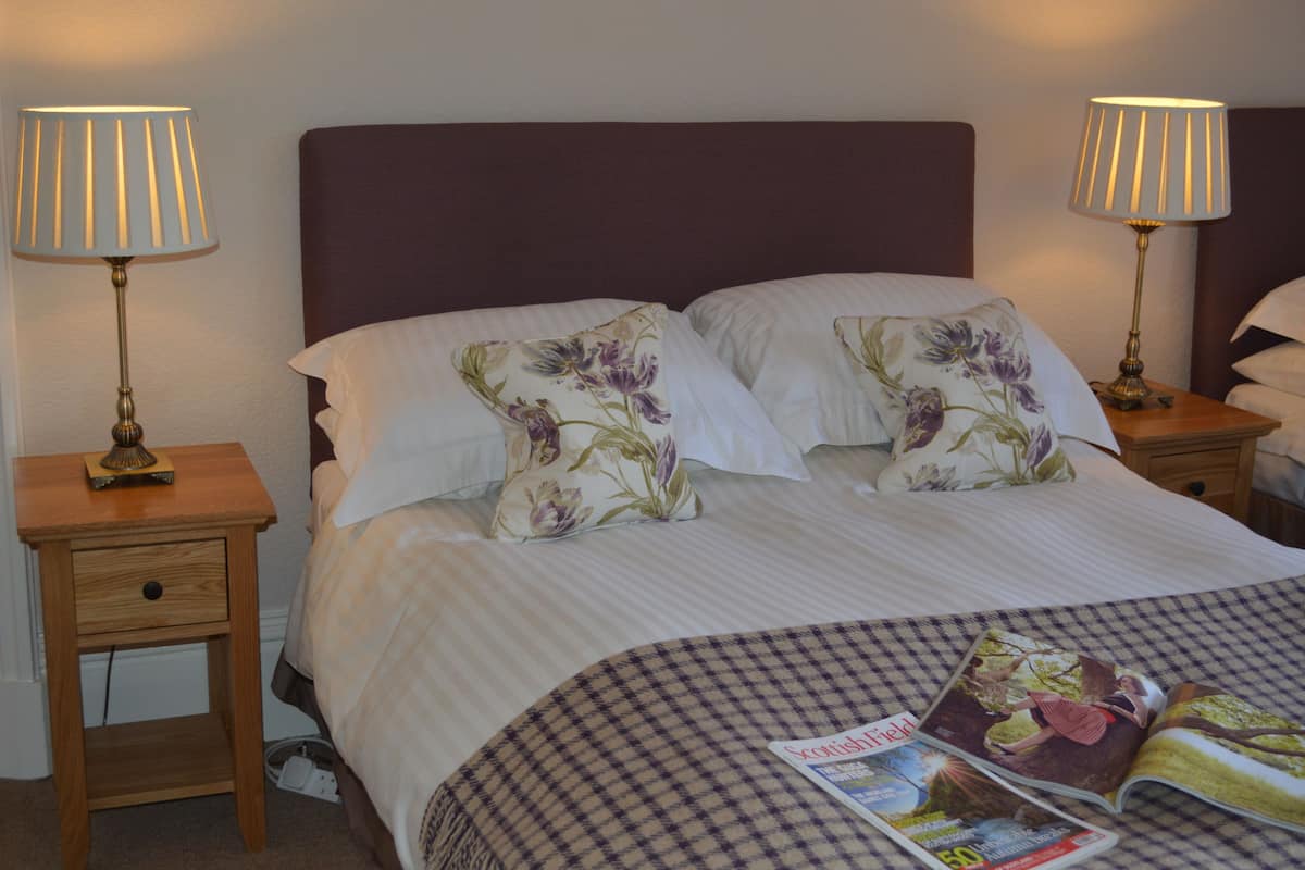 A neatly made bed with floral pillows, two bedside lamps, and a magazine on the bed.