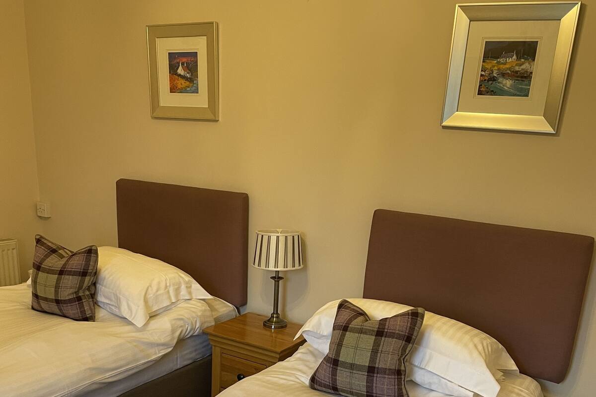A hotel room with two single beds, a nightstand with a lamp, and two framed pictures on the wall.