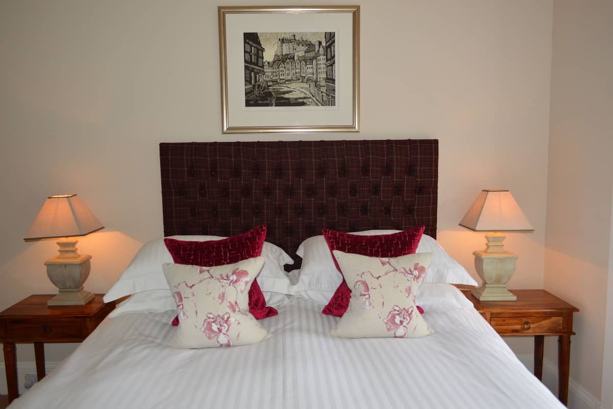 A neatly made bed with a striped bedspread, two pillows with floral designs, and a headboard. There are two bedside tables with lamps, and a framed picture on the wall above the bed.