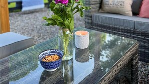 Uma mesa de vidro com um vaso de flores roxas, uma vela e uma tigela de petiscos.