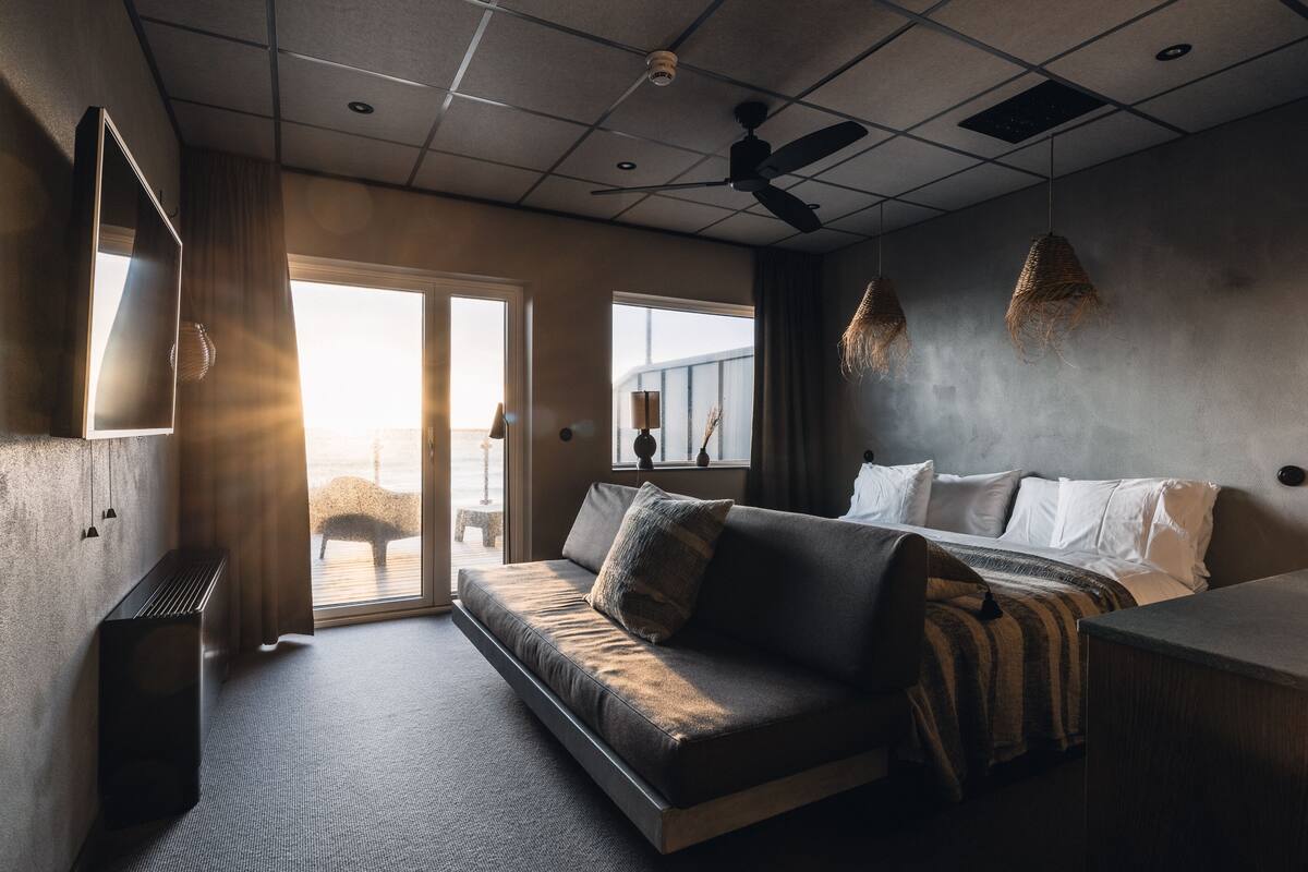 Una habitación de hotel moderna con sofá, cama, ventilador de techo y vistas al exterior.