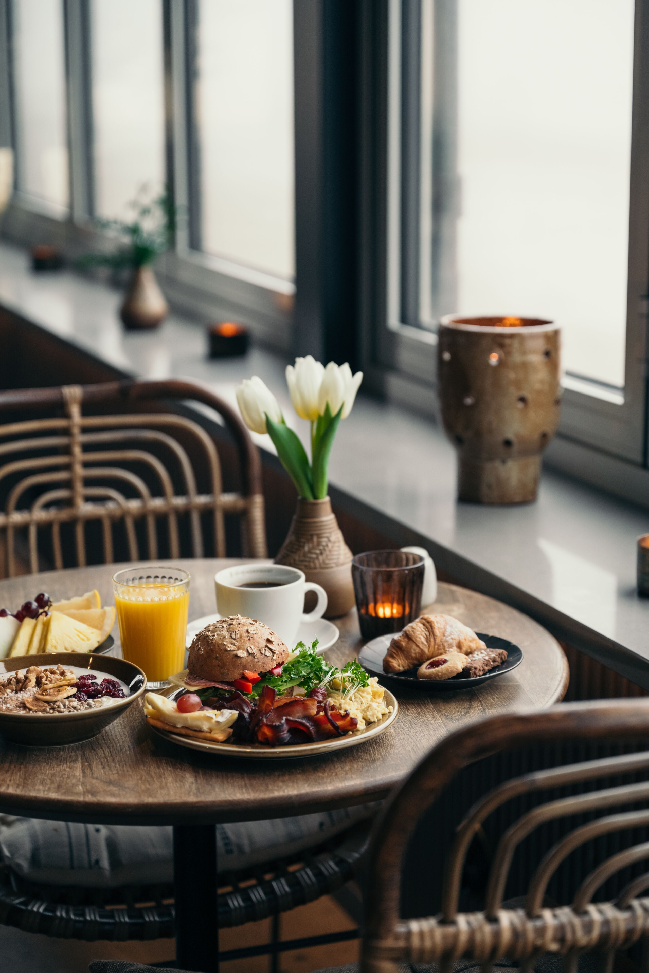 A breakfast table with plates of food, a coffee cup, a glass of orange juice, and a vase with flowers.
