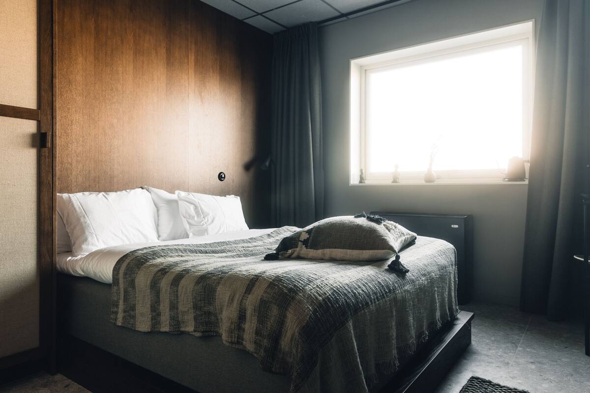 Un dormitorio con cama, ventana con cortinas y un radiador.