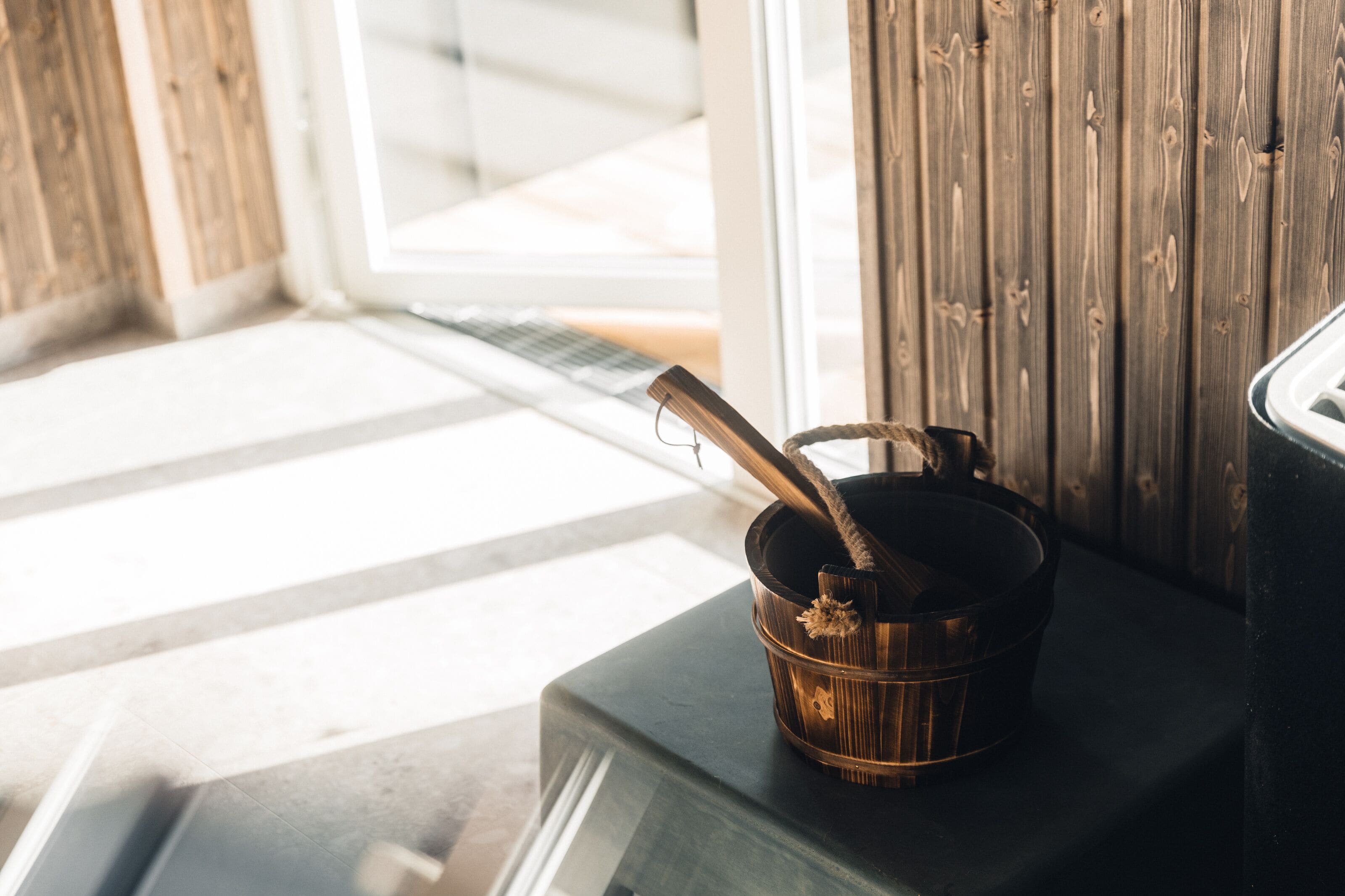 A rustic wooden wall with a metal bucket containing a rope and a metal hook.