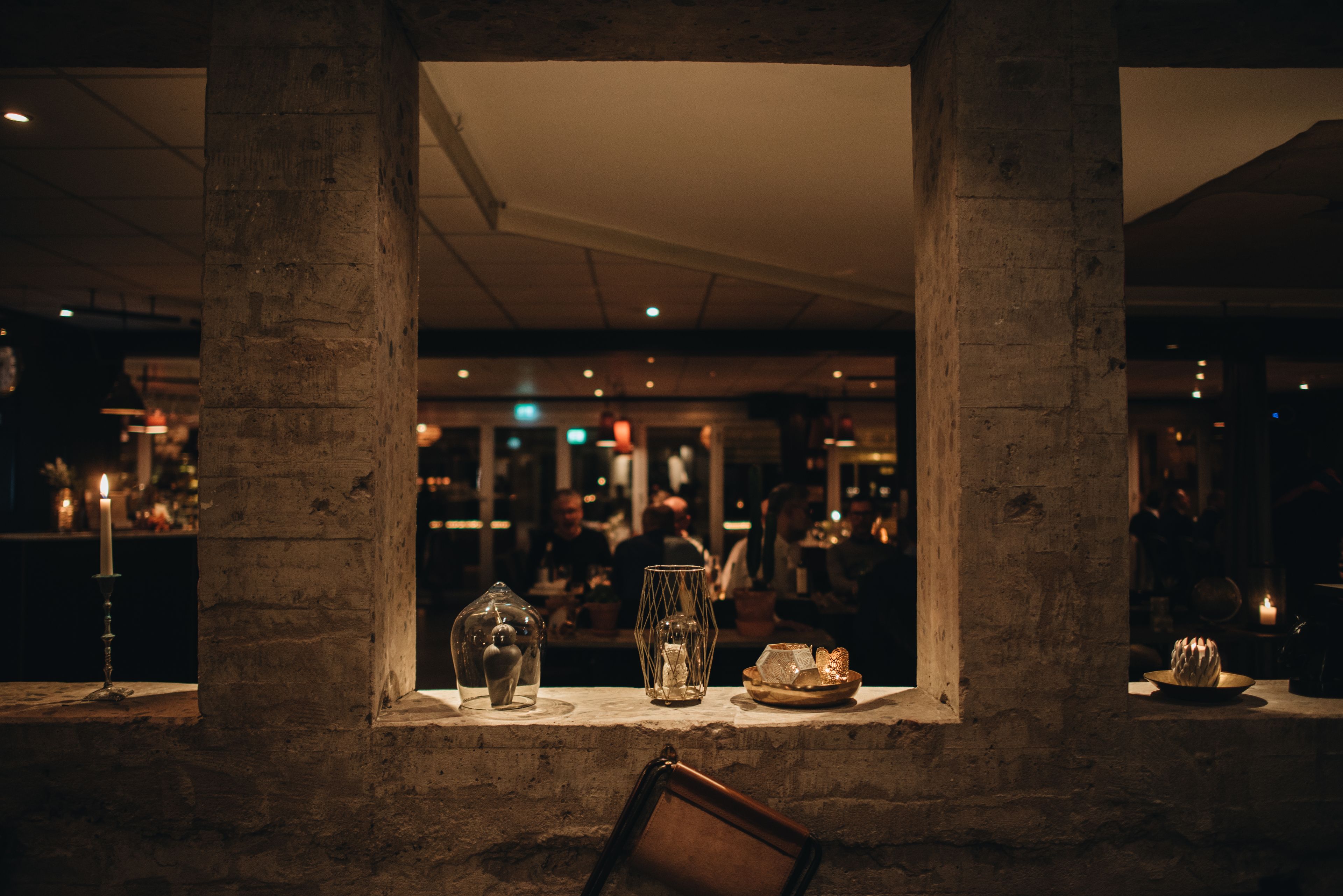A dimly lit interior with a stone column structure, a candle, and a glass vase on a ledge.