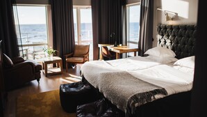A hotel room with a large bed, a desk, a chair, a sofa, and a view of the ocean. - Ocean Hotel (Falkenberg)