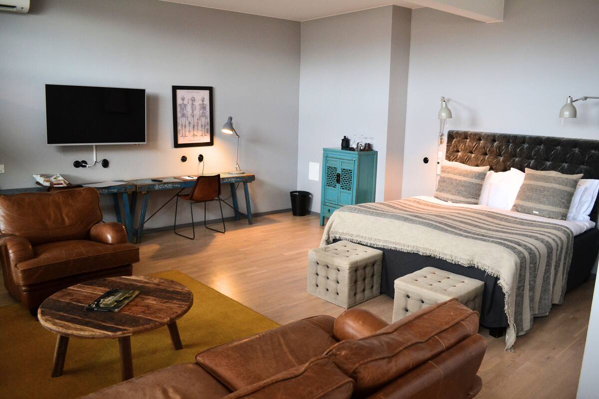 Un dormitorio moderno con una cama grande, un escritorio, una silla y un sofá de cuero.