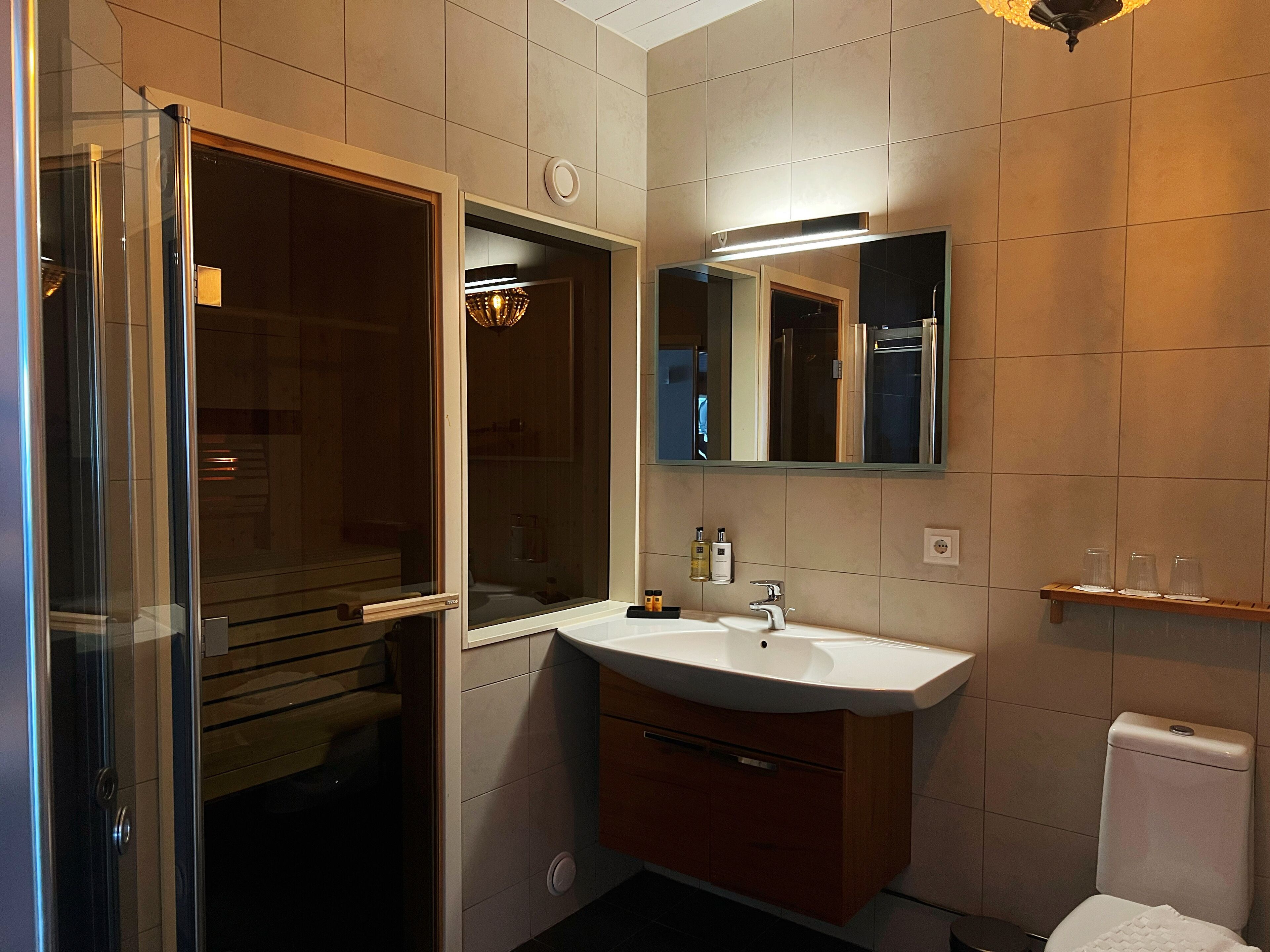 Un baño moderno con cabina de ducha de vidrio, un lavamanos blanco con espejo y un inodoro.