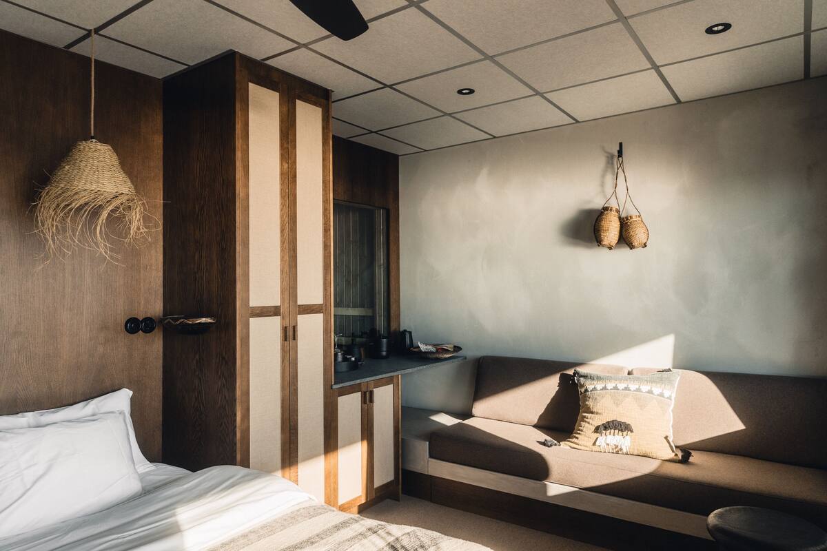 Una habitación moderna con cama, sofá, escritorio pequeño y una cesta colgante.
